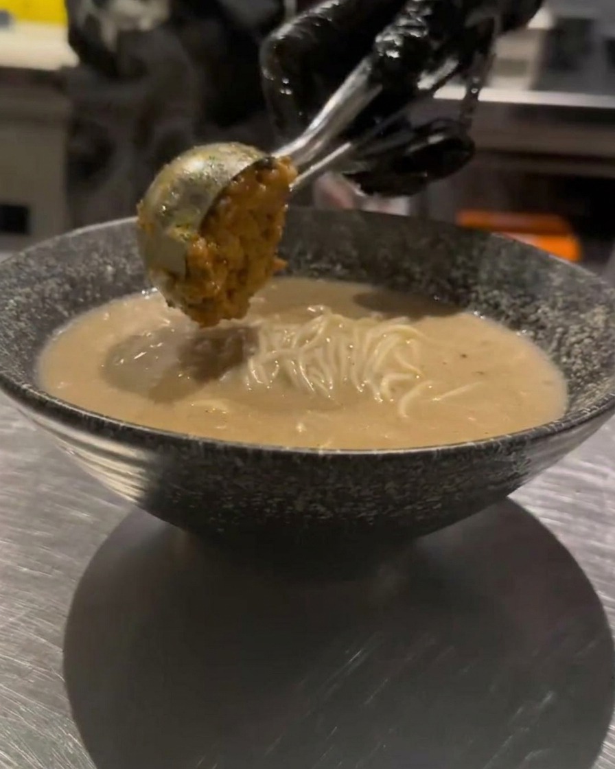 Una cucharada de carne picada sazonada siendo añadida cuidadosamente sobre el ramen.
