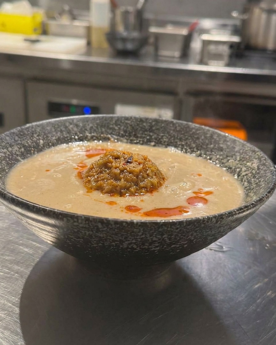 Un tazón de Tan Tan Ramen con caldo cremoso, carne picada y aceite de chile rojo rocíado encima.