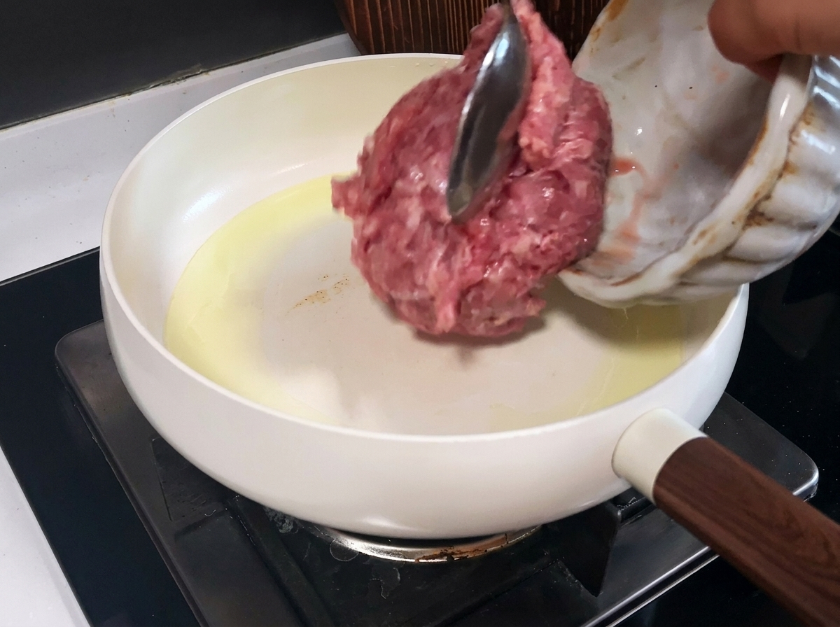 Carne de cerdo picada cocinándose en una sartén blanca, mostrando trozos dorados y cocidos.