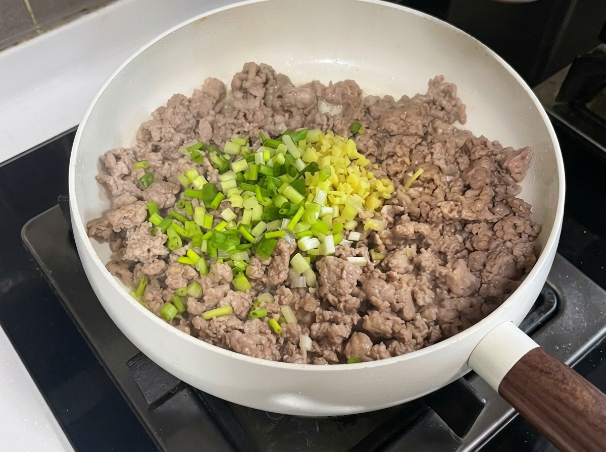 Carne de cerdo picada en una sartén mezclándose con los aromáticos picados, la pasta de judías y la pasta de soja.