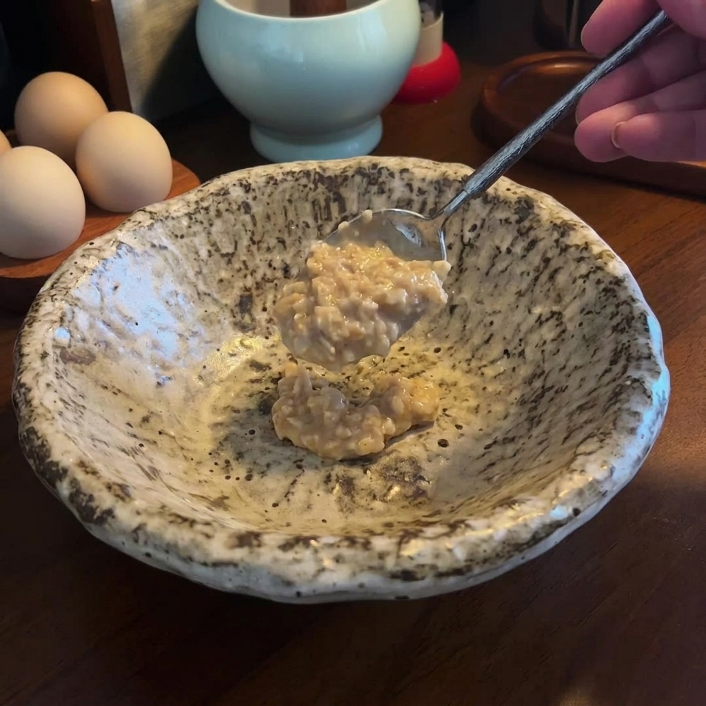 Una cucharada de miso espeso y pasta de sésamo que se añade a un tazón de cerámica moteado vacío.