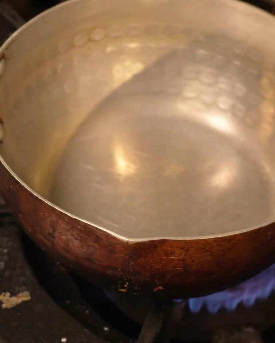 Una olla de metal martillado llena de líquido calentándose sobre el fuego.