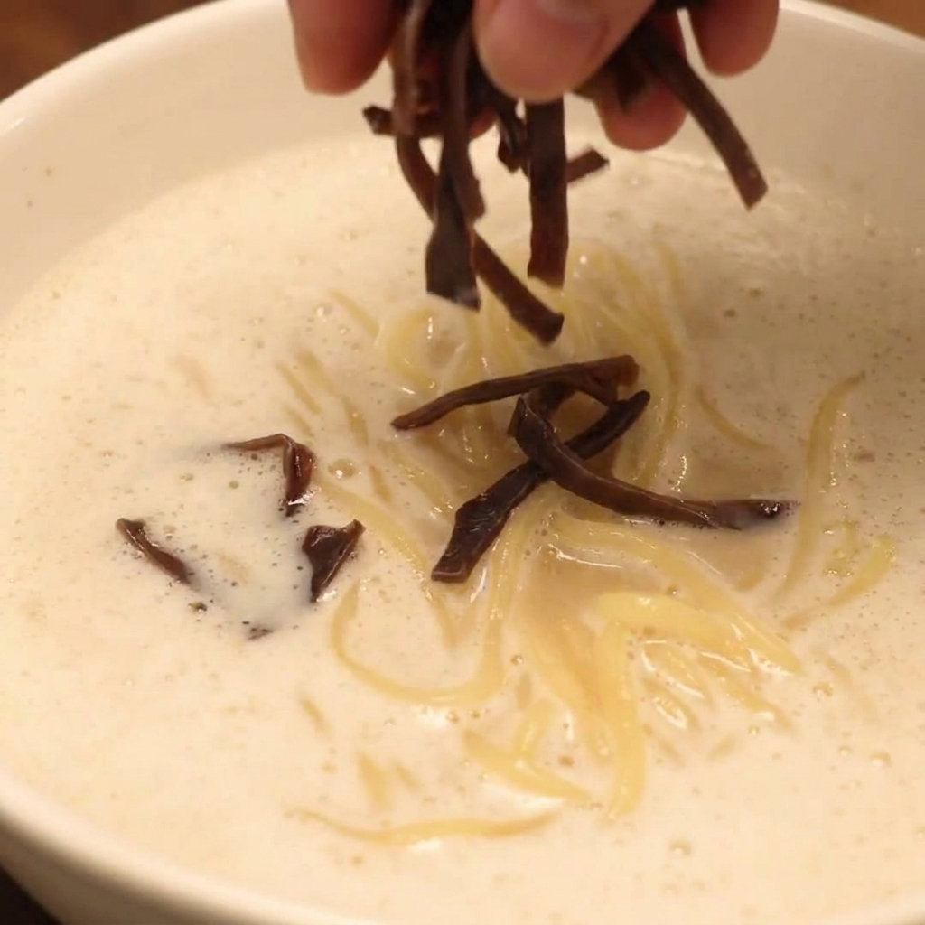 Un tazón completamente ensamblado de Ramen de Pollo Paitan con Espuma decorado con chashu, setas y verduras frescas.