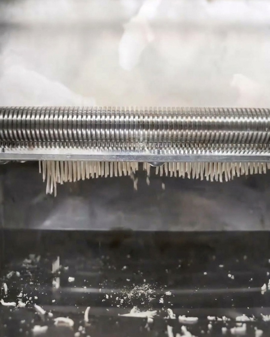 Máquina de fideos prensando y cortando la masa en finas tiras de ramen.