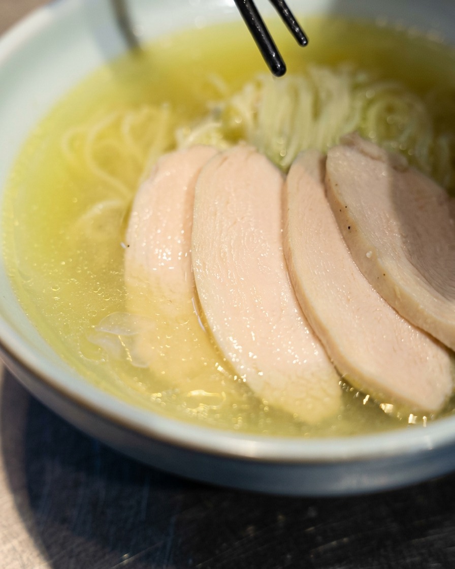 Palillos colocando rodajas de tierno chashu de pollo sobre el ramen recién preparado en un tazón.