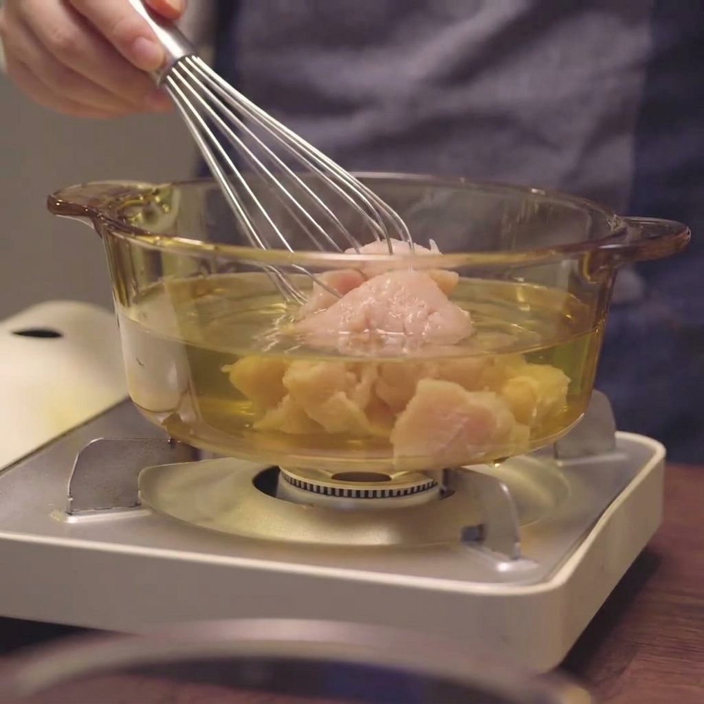 Un batidor mezclando pechuga de pollo picada en el líquido dentro de una olla de cristal.