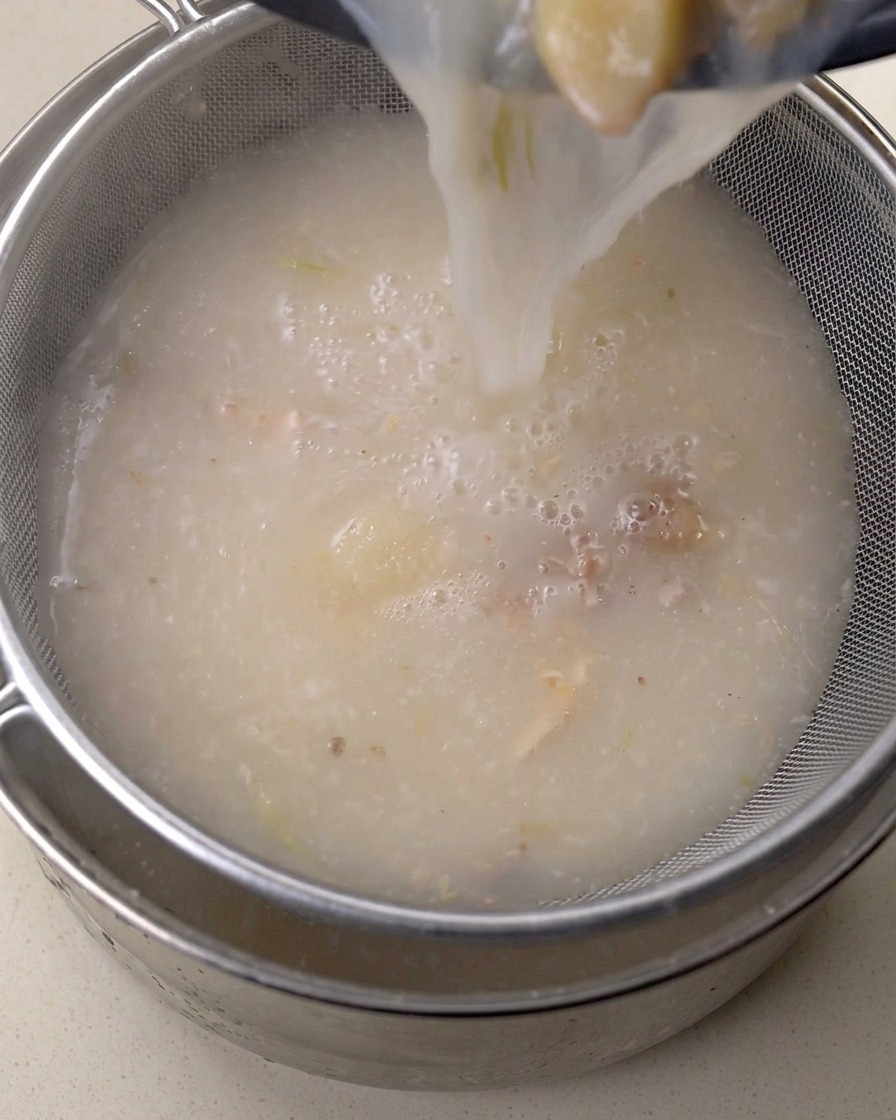 Caldo rico siendo vertido a través de un colador de malla fina.