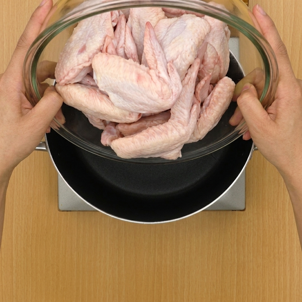 Alitas de pollo y aromáticos siendo añadidos a una olla grande llena de agua.