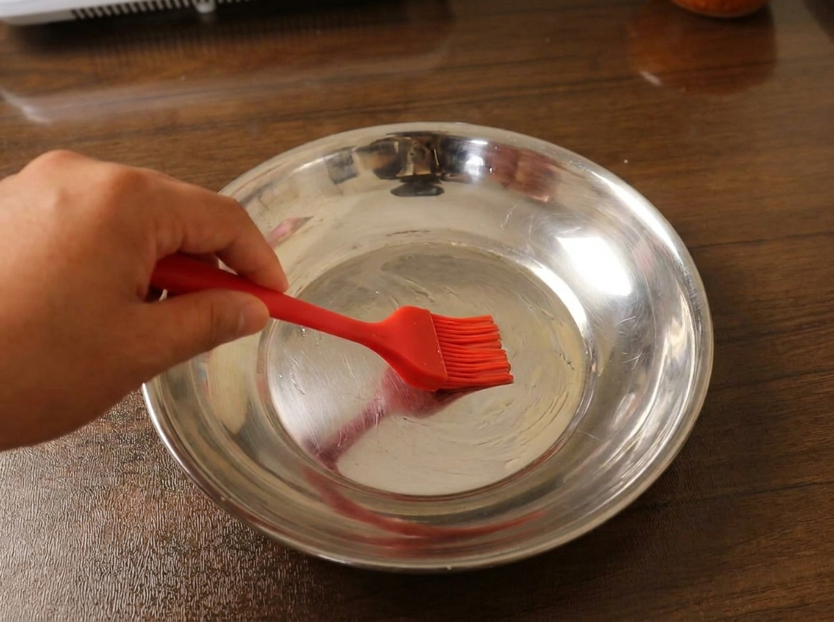 Una capa fina de masa extendida de manera uniforme en un plato de metal, lista para ser cocinada al vapor.