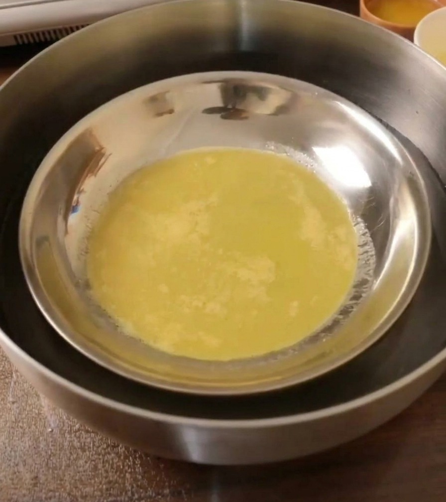 Una lámina de masa elástica y cocida dentro de un plato de metal enfriándose en un baño de agua.