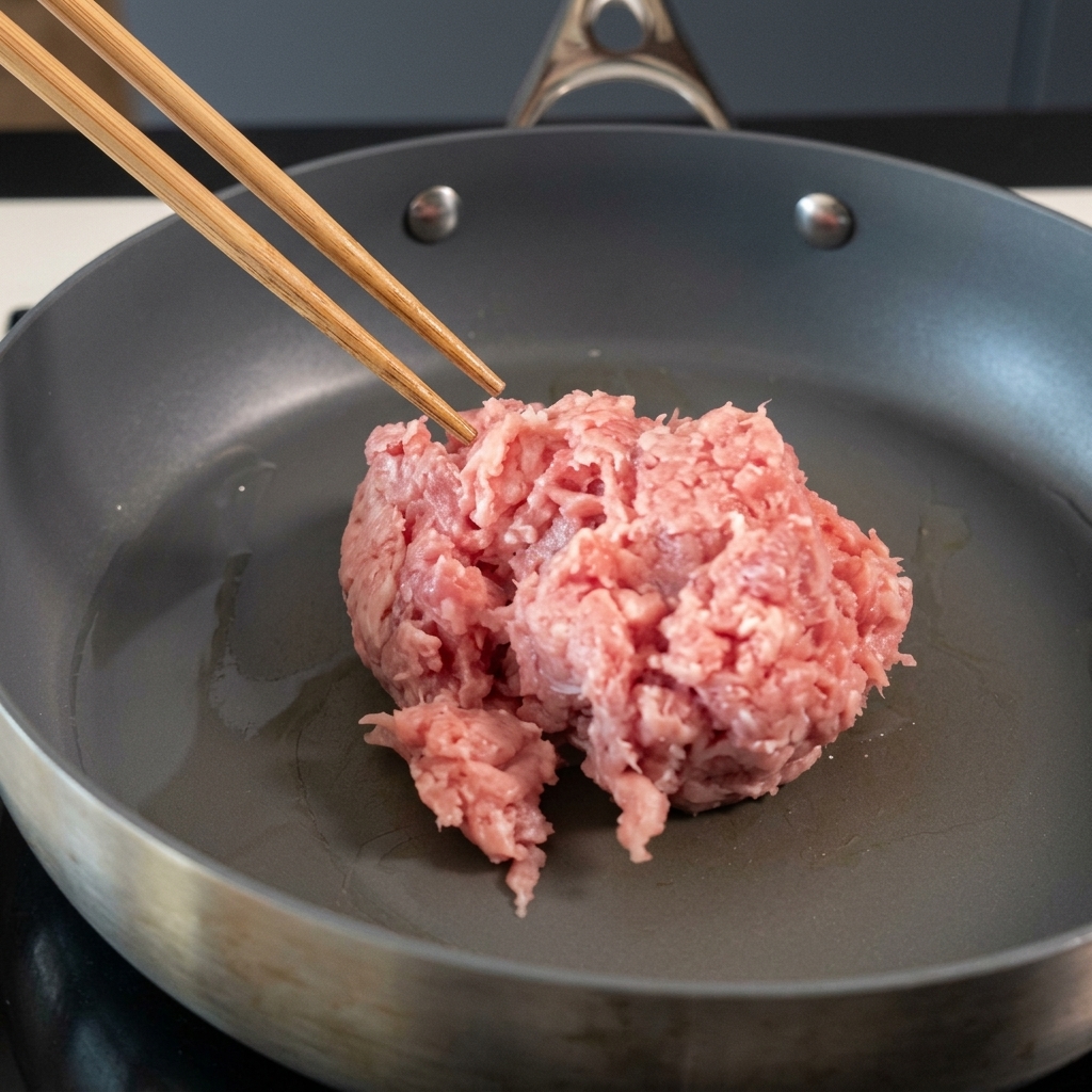 Carne de cerdo picada siendo salteada en una sartén antiadherente con palillos.
