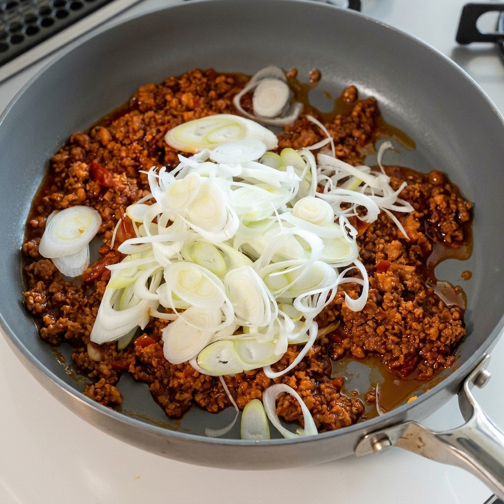 Un montón de cebolletas picadas siendo añadidas a la salsa de carne.