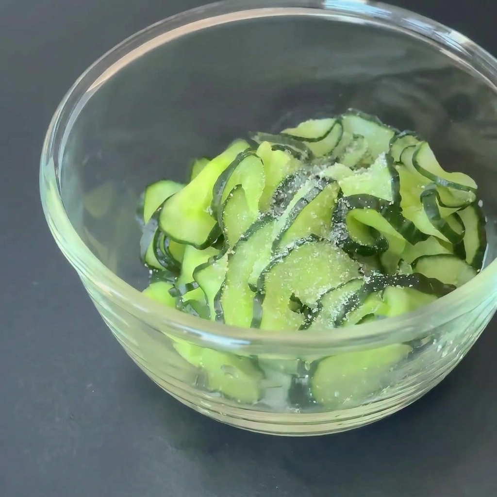 Rodajas de pepino en un tazón de vidrio sazonadas con azúcar y vinagre de manzana.