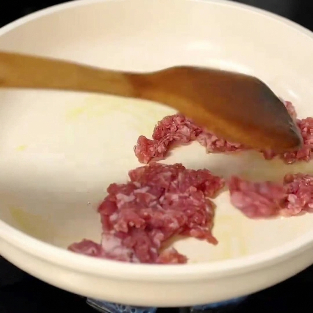 Carne de cerdo picada siendo salteada en una sartén con una espátula de madera.