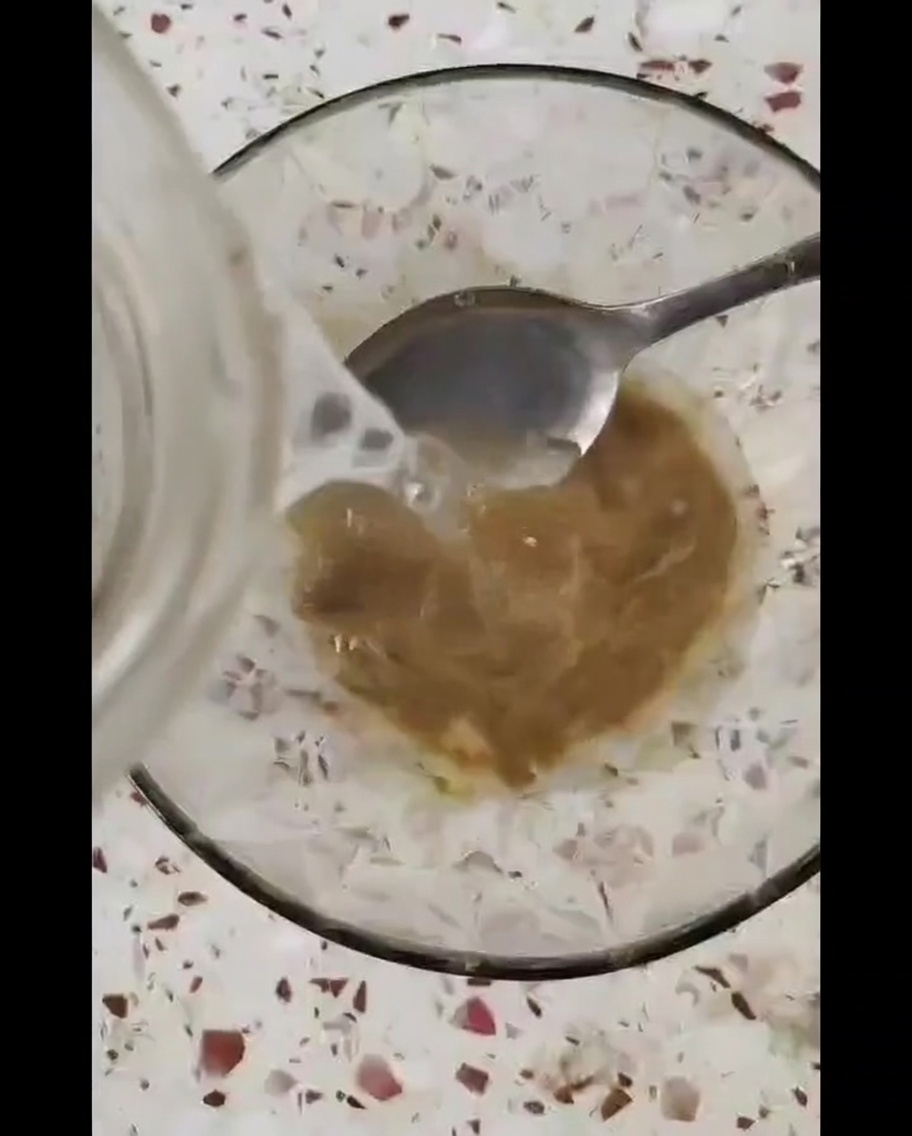 Un pequeño tazón de vidrio que contiene una salsa espesa de color marrón siendo revuelta con una cuchara de metal.