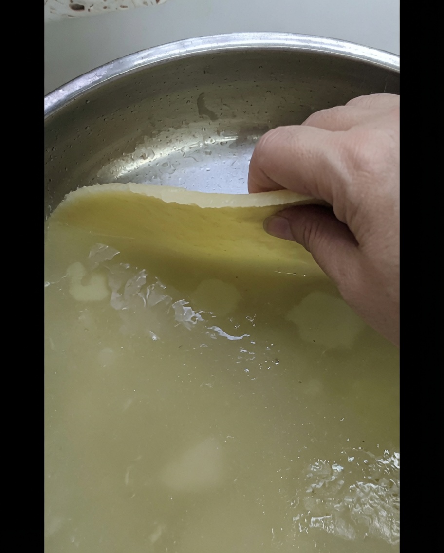 Una mano colocando una hoja de masa estirada sobre una bandeja de metal brillante.