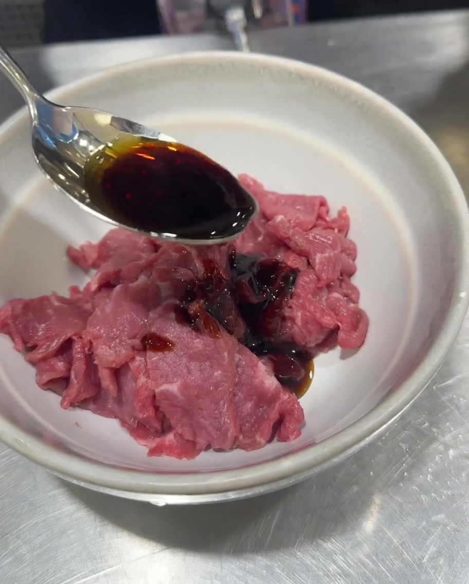 Ternera cruda en un bol siendo sazonada con salsa de soja, sal, pimienta y almidón de maíz.