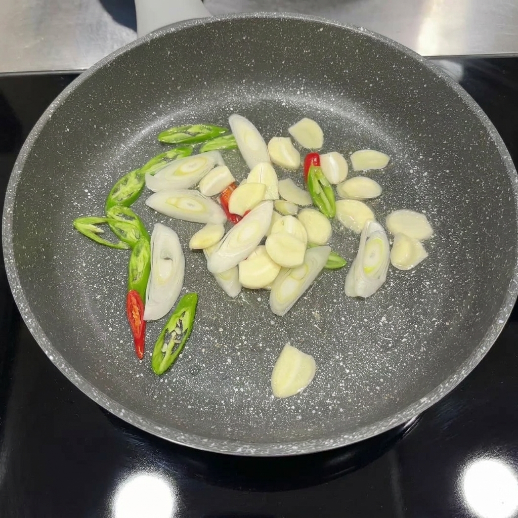 Ajo, chiles y cebolleta picados cocinándose en una sartén hasta estar aromáticos.