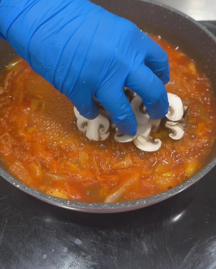 Champiñones shiitake, calabacín y tofu siendo añadidos a la base de sopa hirviendo.