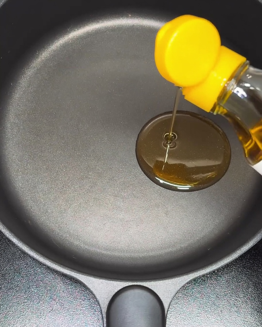 Aceite de sésamo vertiéndose en una sartén antiadherente.