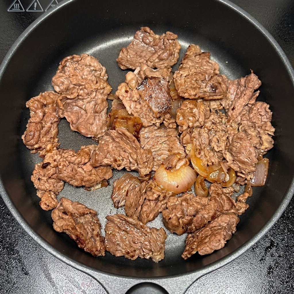 Trozos de kimchi mezclándose en la sartén con la ternera y la cebolla.