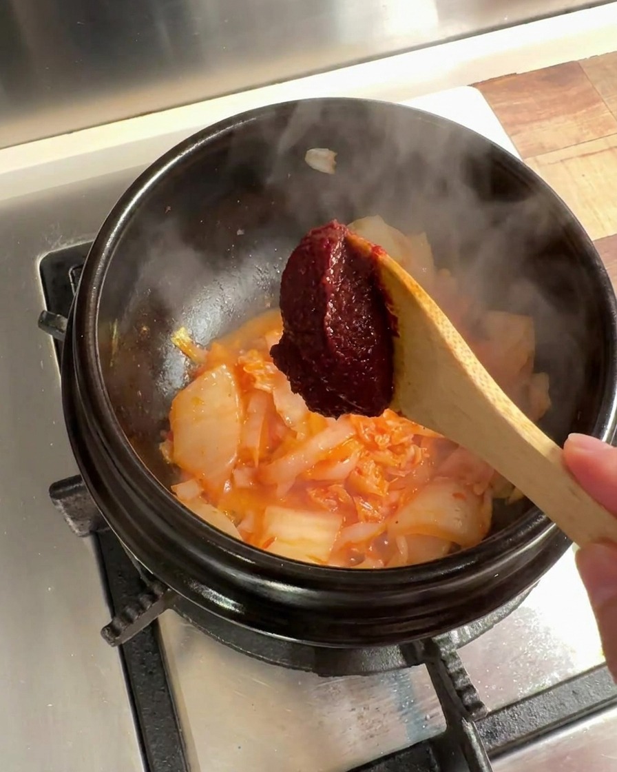 Una cucharada de pasta de chile coreana añadida a la mezcla de kimchi y cebolla en la olla.