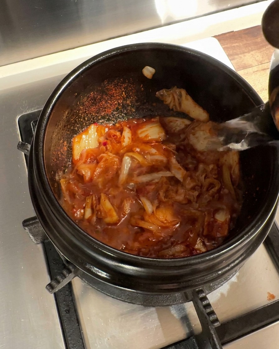 Agua caliente vertida en la olla de barro con la base de kimchi y cebolla sazonada.
