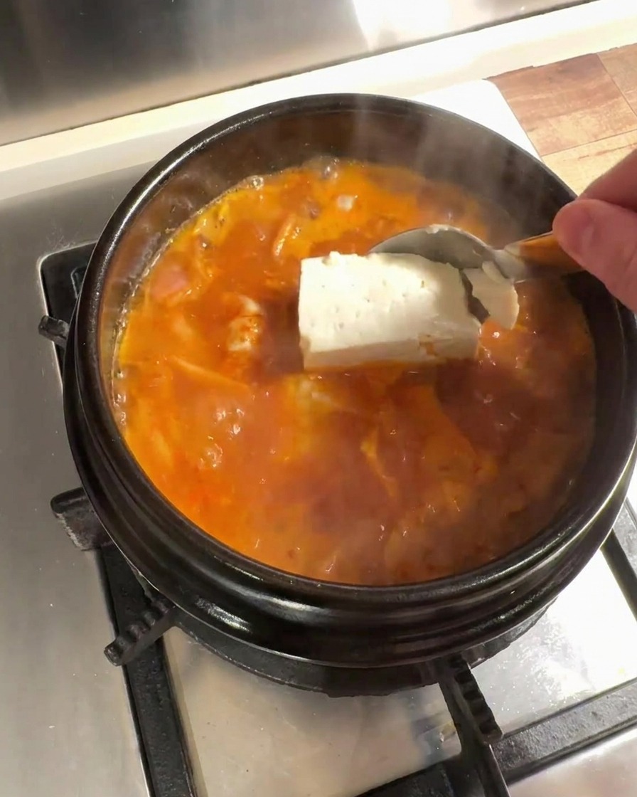 Grandes trozos de tofu fresco añadidos al caldo de kimchi en ebullición.