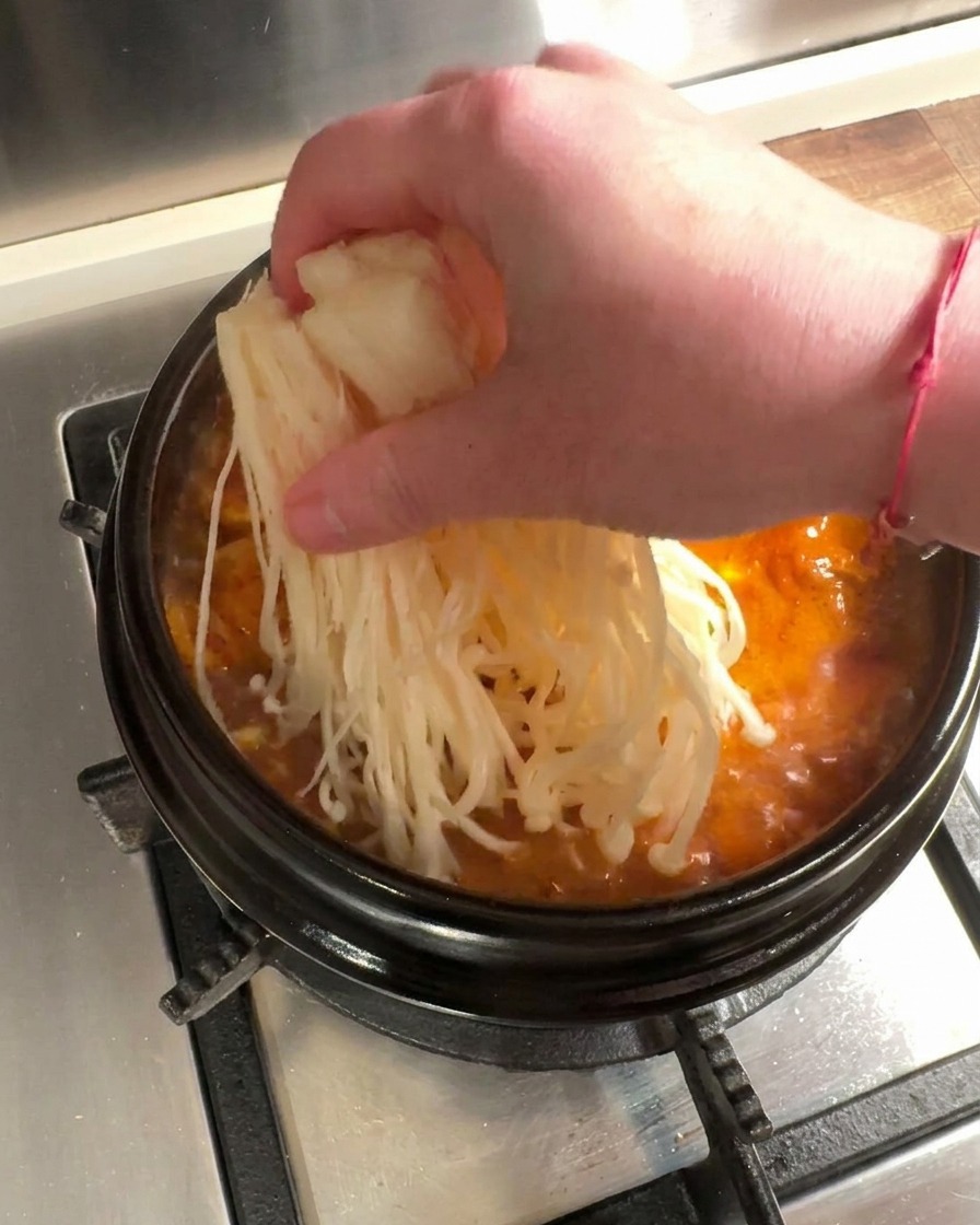 Setas enoki frescas y ternera en láminas finas colocadas en un estofado de kimchi hirviendo.