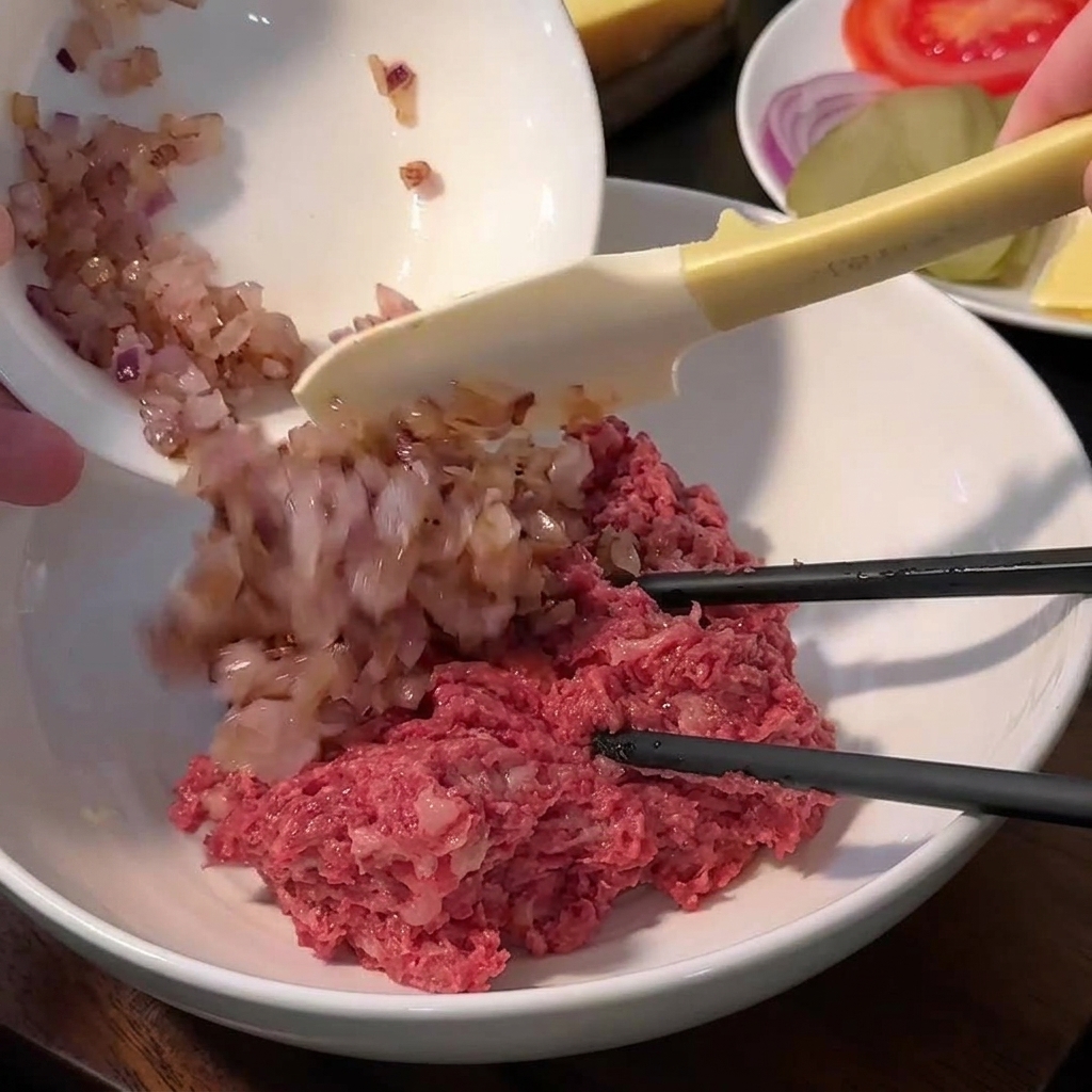 Un bol con carne molida, pan rallado, sal, pimienta y cebollas salteadas antes de mezclar.
