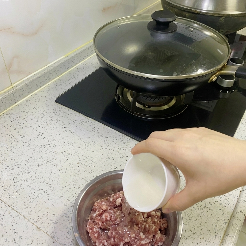 Agua de cebolla y jengibre siendo vertida en un tazón con carne picada cruda.