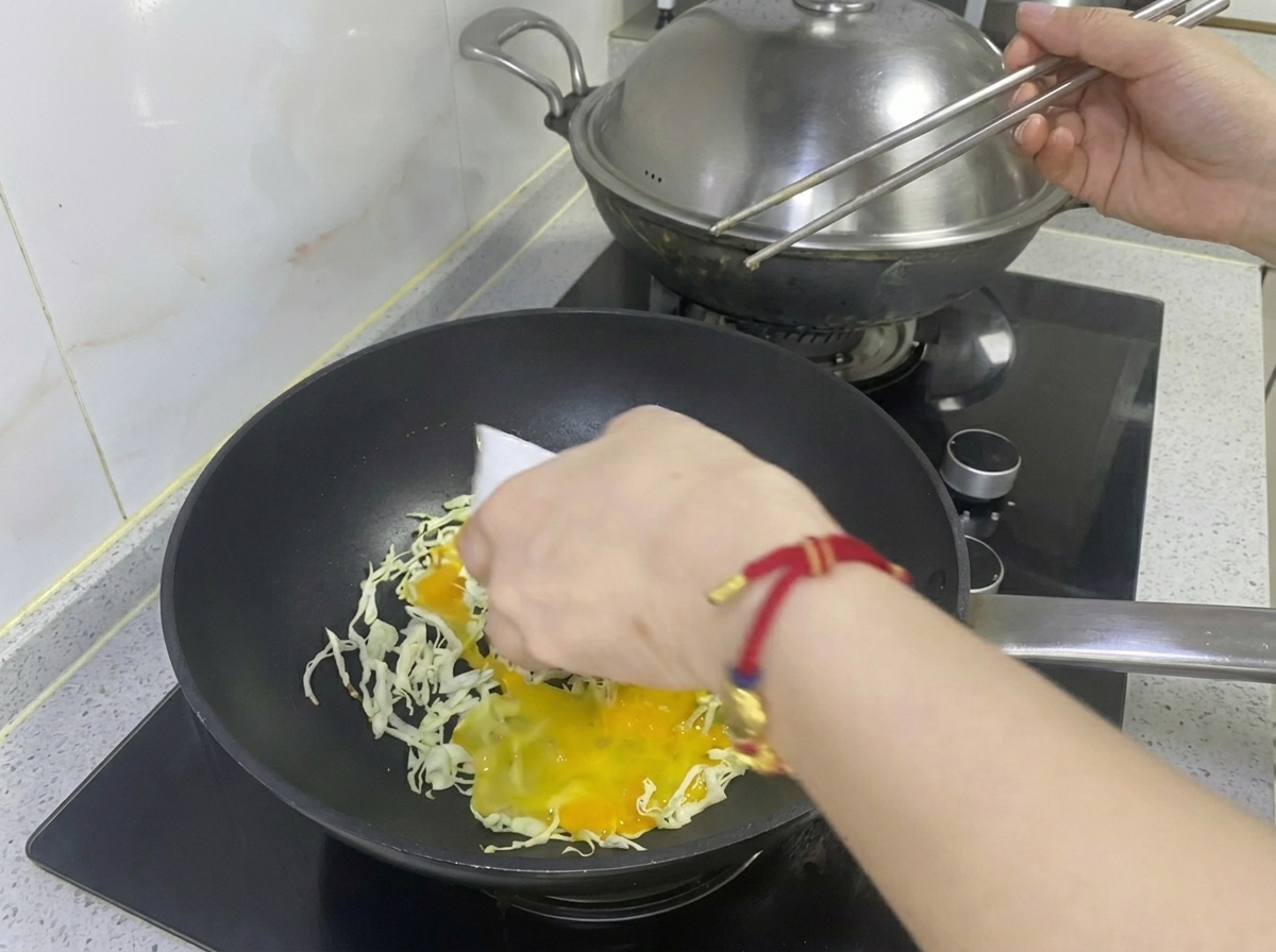 Huevo batido siendo vertido sobre el repollo rallado en la sartén.