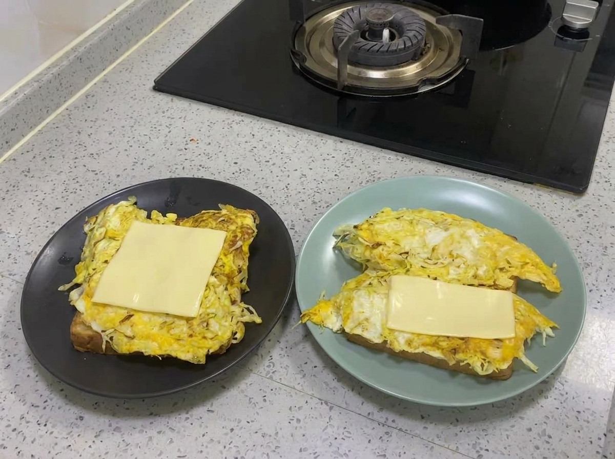 Una rebanada de queso amarillo derritiéndose sobre la capa cocida de huevo y repollo.