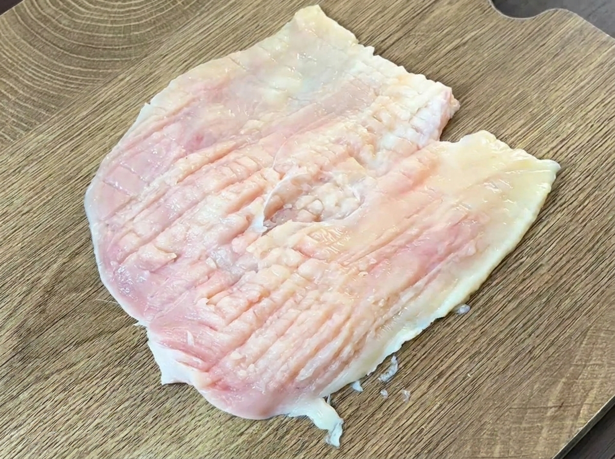 Parte posterior de un cuchillo pesado siendo usada para golpear y aplanar una pechuga de pollo mariposeada.