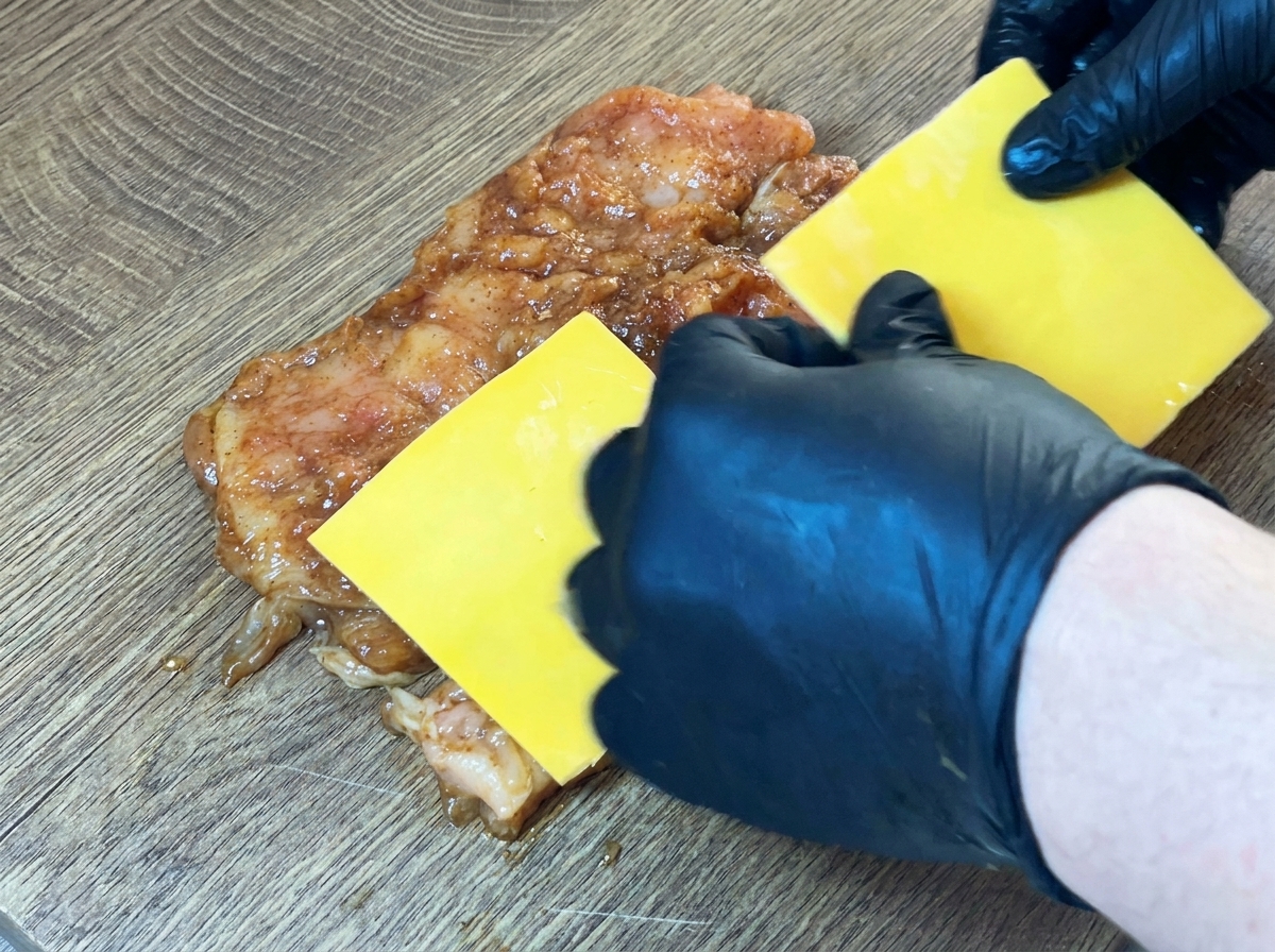 Lonchas de queso amarillo colocadas en el centro de la pechuga de pollo cruda y marinada.