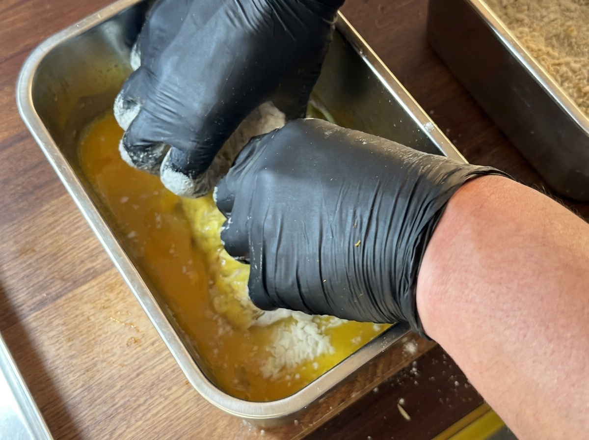 Pieza de pechuga de pollo siendo sumergida completamente en un recipiente con mezcla de huevo batido.