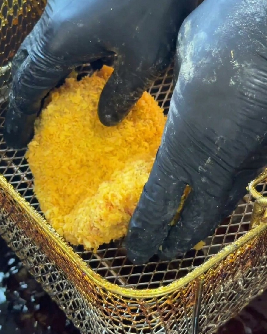 Patty de pollo empanado siendo sumergido en aceite caliente para freír.