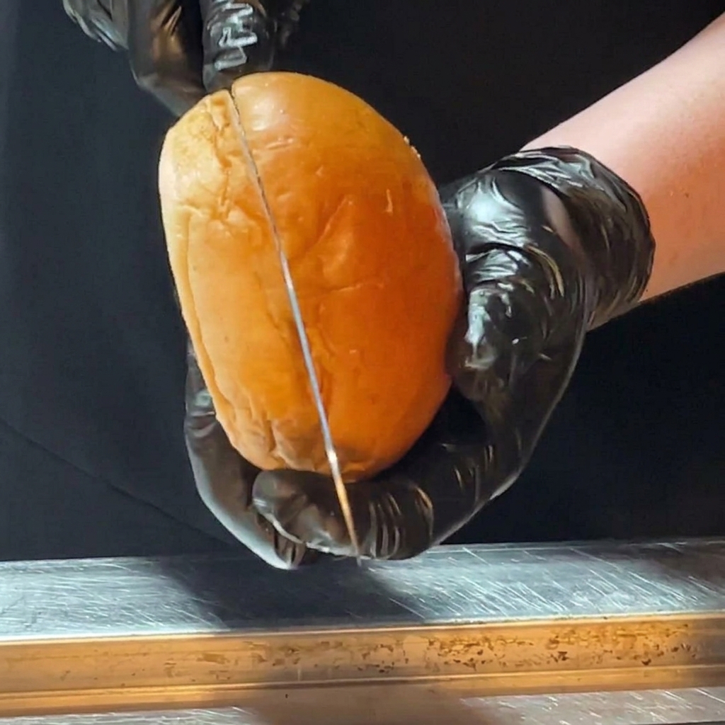 Manos con guantes de cocina negros cortando un pan brioche brillante por la mitad con un cuchillo largo.