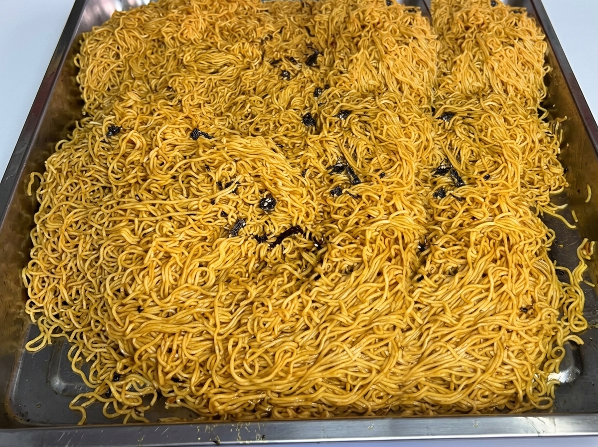 Una gran cantidad de fideos cocidos extendidos en una bandeja de acero inoxidable.