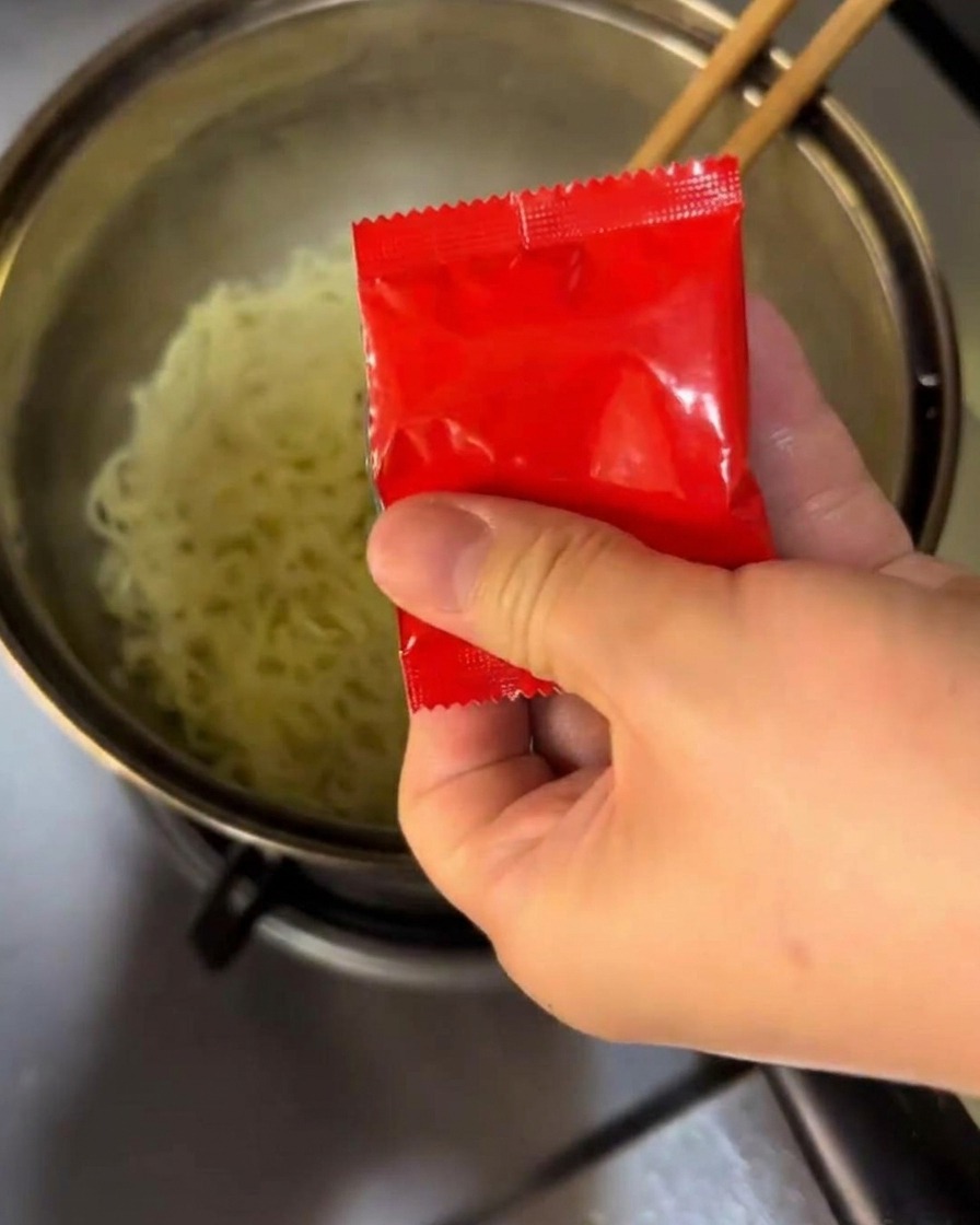 Mezclando el condimento y la salsa picante en fideos hirviendo en una olla.