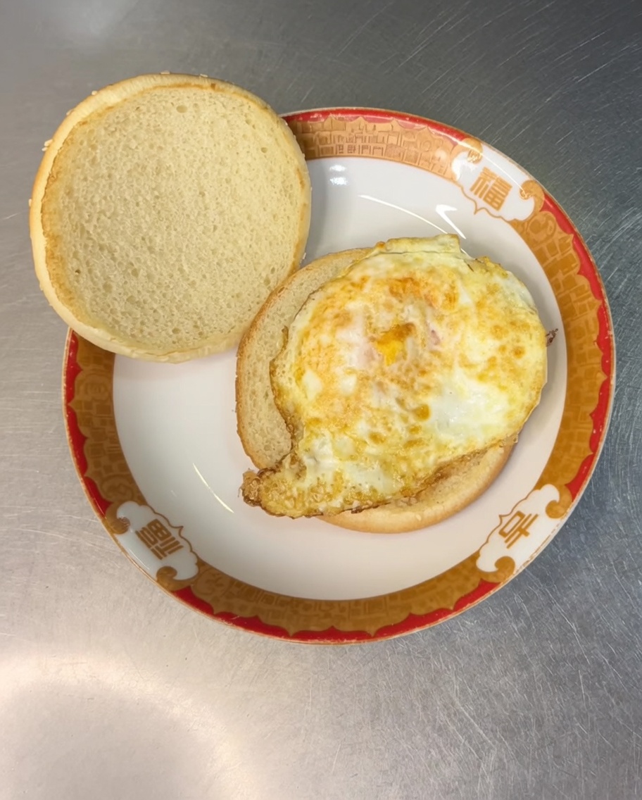 Una loncha de queso amarillo colocada sobre el huevo frito dentro del pan.
