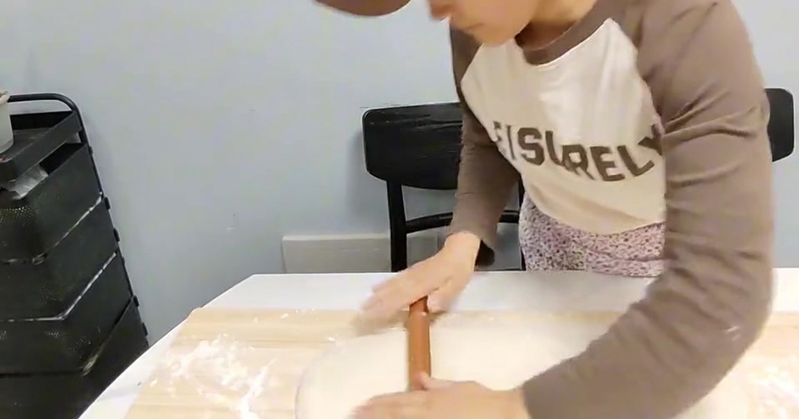 Persona usando un rodillo de madera para aplanar un bloque de masa sobre una tabla de madera enharinada.