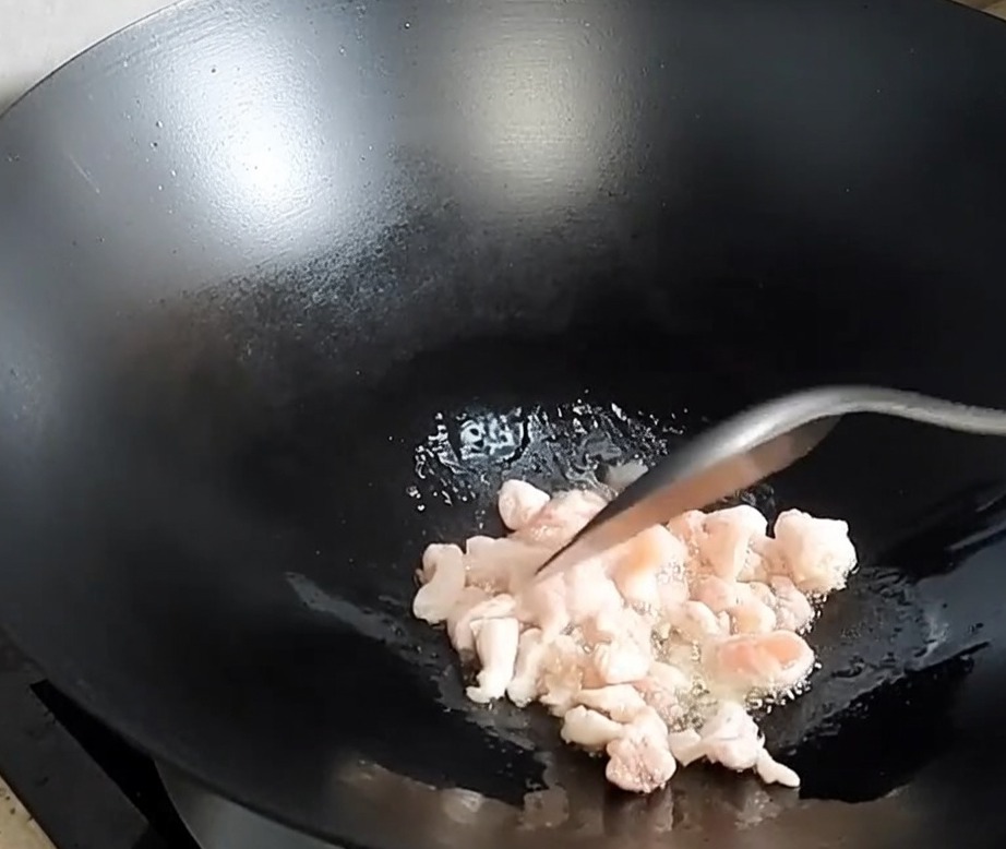 Dados de panceta de cerdo dorándose y soltando grasa en un wok caliente.
