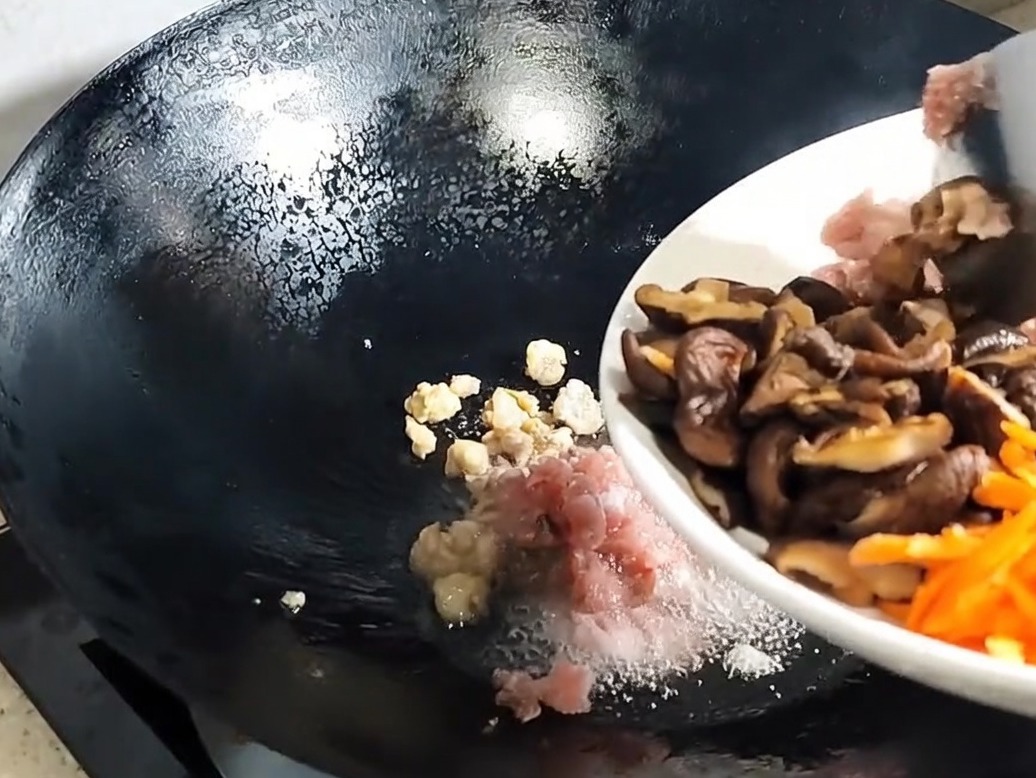 Hongos shiitake rebanados y aromáticos siendo añadidos al cerdo en el wok.