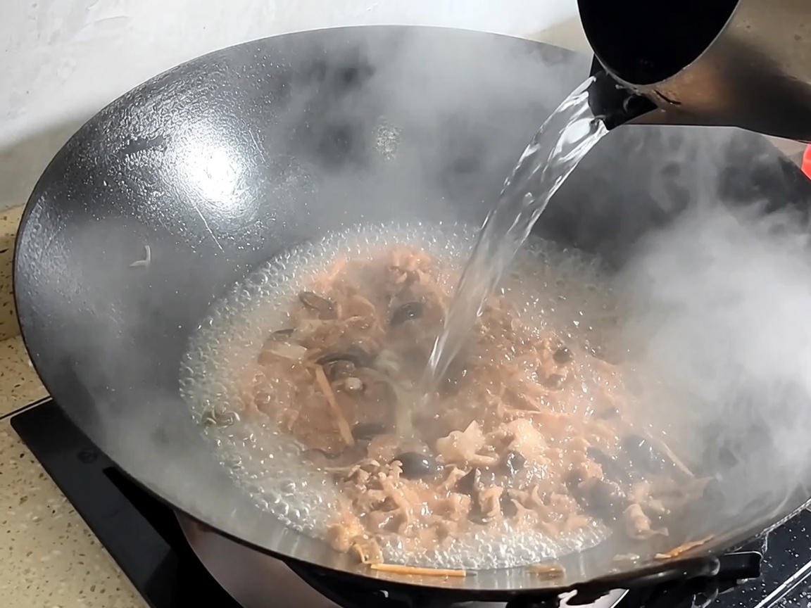 Agua vertida en el wok con cerdo y hongos salteados para formar el caldo.