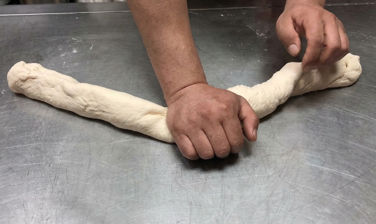 Masa siendo estirada y amasada en forma de cuerda larga sobre una superficie de acero inoxidable.