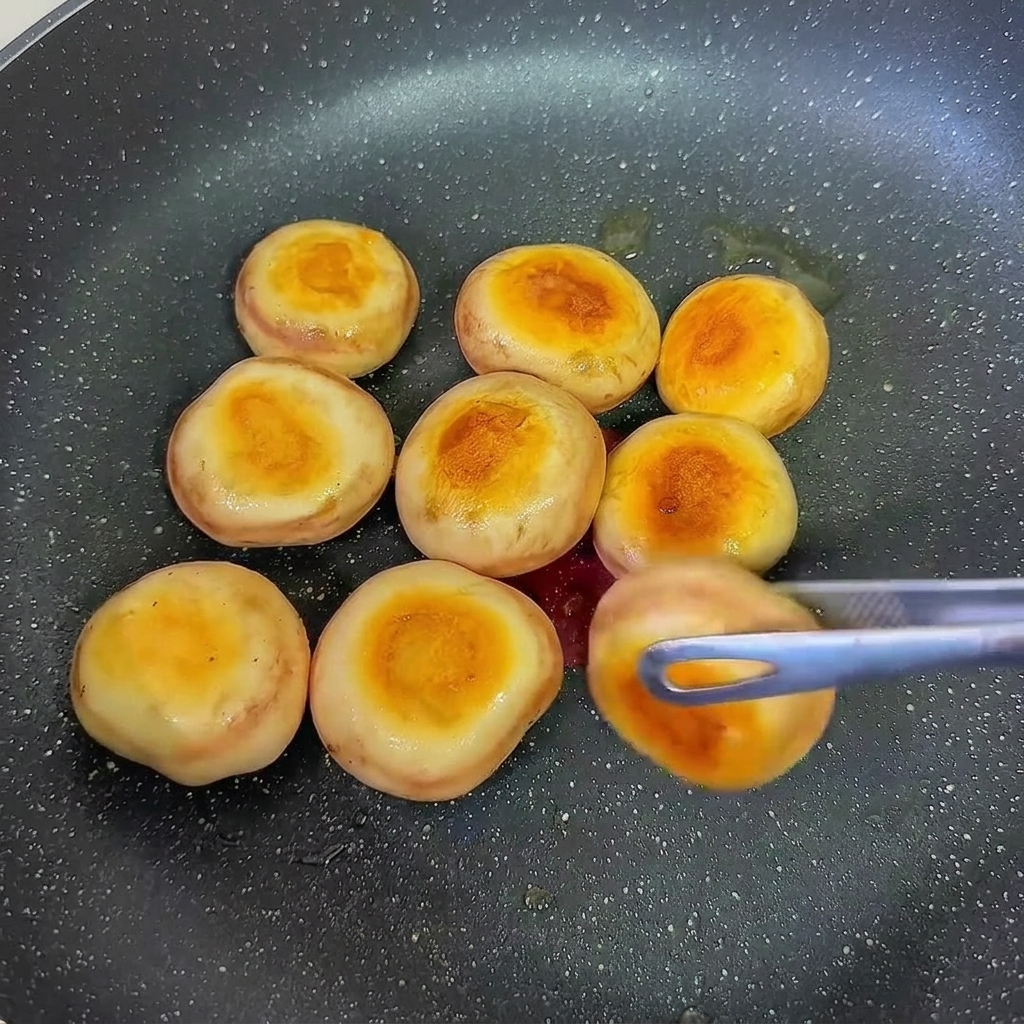 Champiñones rellenos de pasta de camarón friéndose en una sartén, siendo volteados para dorar el otro lado.