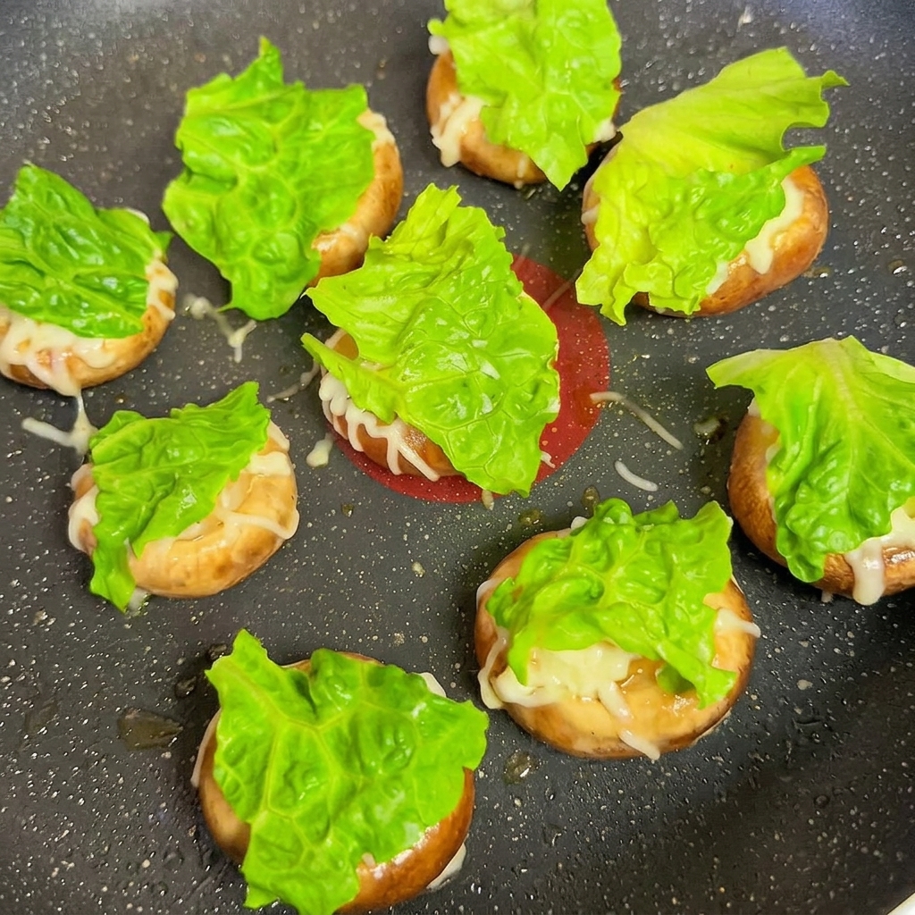 Sombreros de champiñón cubiertos con lechuga y cuadros de queso en una sartén.