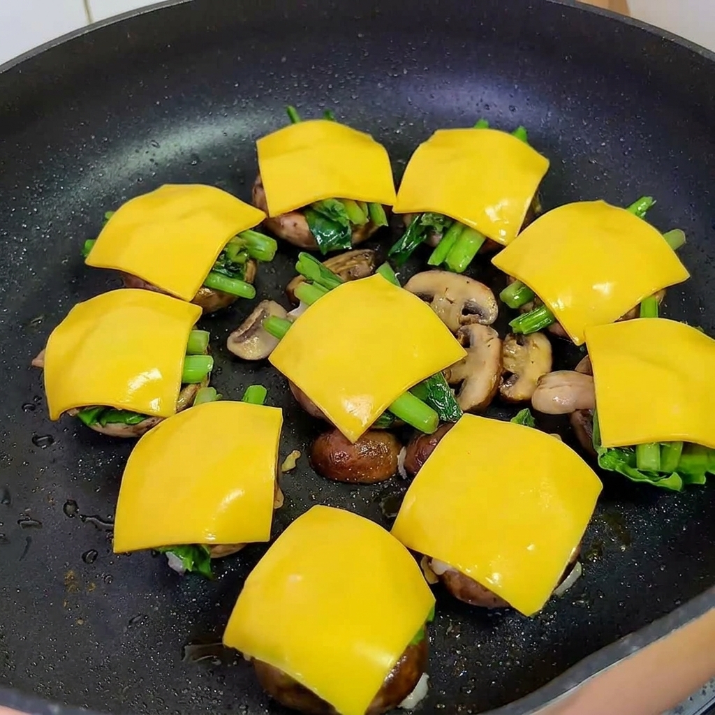 Sartén cubierta con una tapa, cocinando al vapor las hamburguesas de champiñón para derretir el queso.