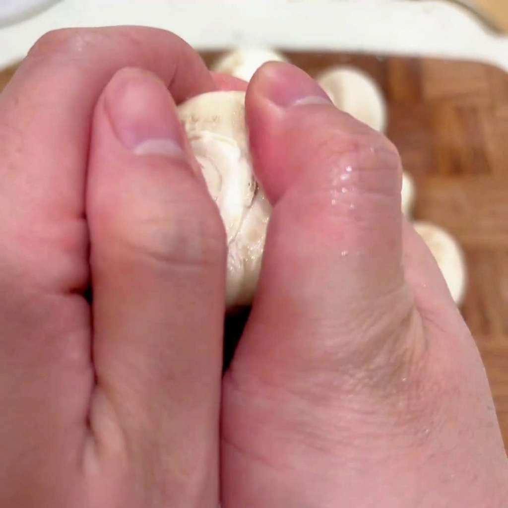 Primer plano de manos retirando el tallo de un champiñón blanco fresco para prepararlo para el relleno.